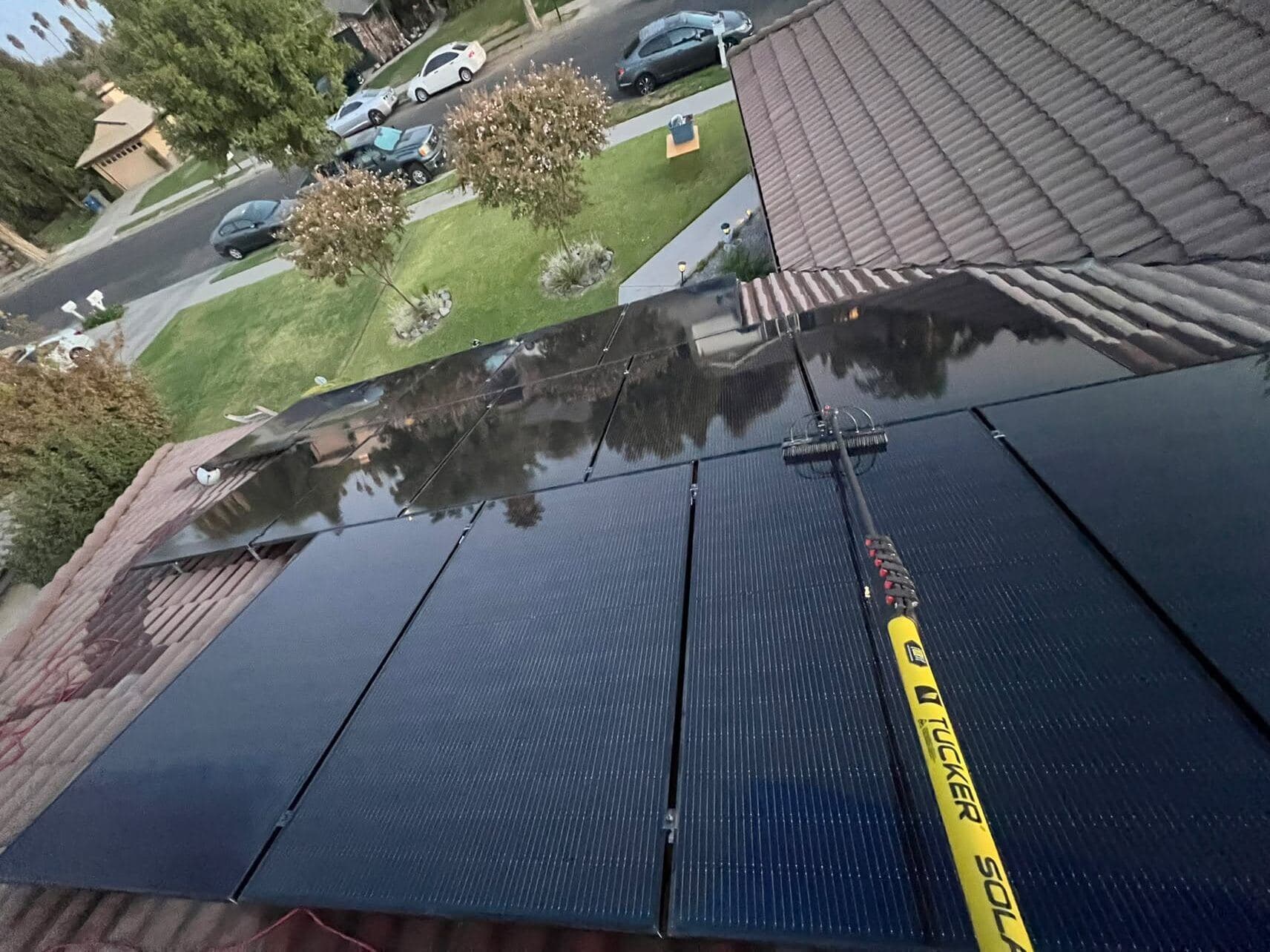 Water-fed pole with a soft brush cleaning solar panels on a tile roof at golden hour